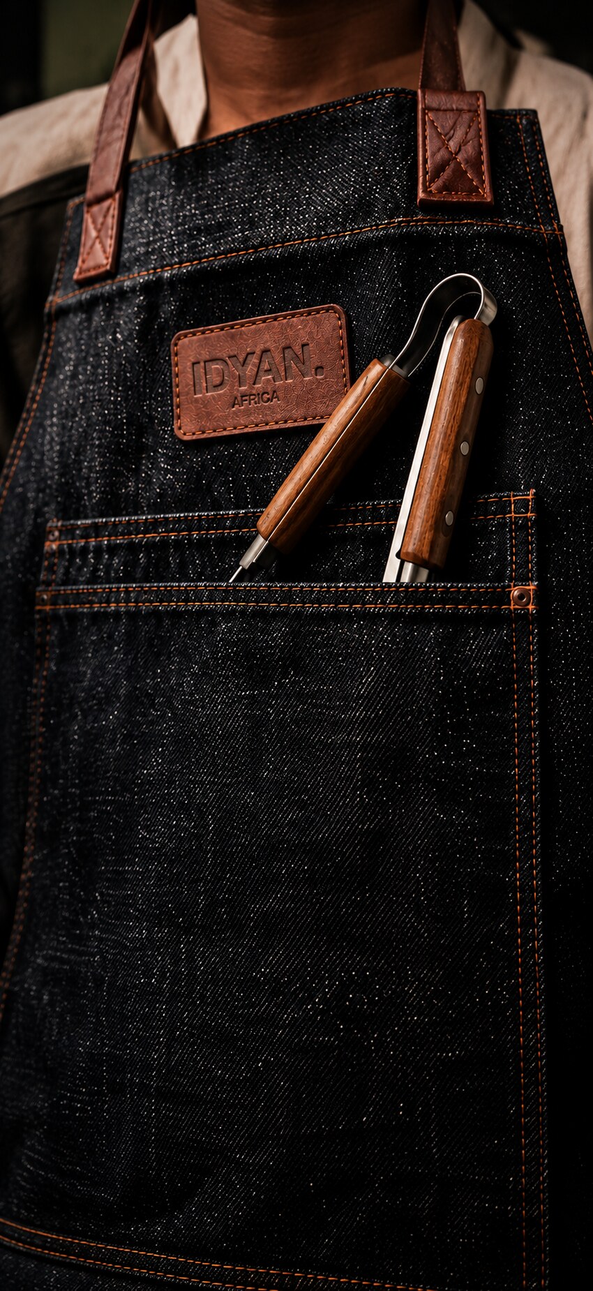 IDYAN denim apron worn with braai tongs in the chest pocket